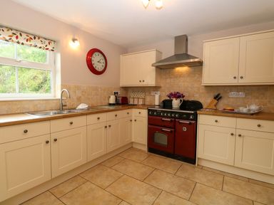 A kitchen with cream cabinets a red stove and a clock on the wall at Dairy Cottage in West Caister near Caister-on-Sea