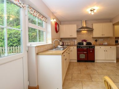 A kitchen with white cabinets a red oven a sink under a window and tiled floor at Dairy Cottage in West Caister near Caister-on-Sea
