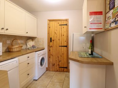 A utility room with a washing machine dishwasher wooden door and wine bottle at Dairy Cottage West Caister near Caister-on-Sea