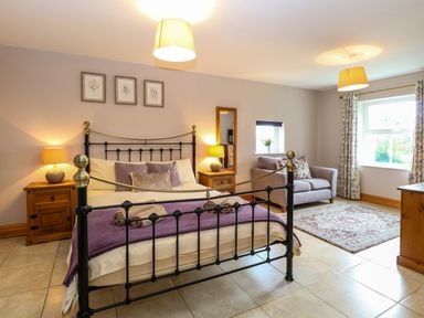 A bedroom with a metal bed frame bedside tables with lamps sofa and windows with floral curtains at Dairy Cottage in West Caister near Caister-on-Sea