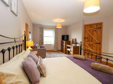 A bedroom with a bed sofa wooden door wooden dresser and a desk at Dairy Cottage in West Caister near Caister-on-Sea