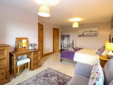 A bedroom with a bed a dressing table a sofa and wooden doors at Dairy Cottage in West Caister near Caister-on-Sea