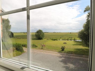 A view of a green field with a picnic bench and trees seen through a window at Dairy Cottage in West Caister near Caister-on-Sea