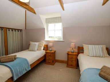 A bedroom with two single beds with blue throws and wooden bedside tables with lamps at Dairy Cottage in West Caister near Caister-on-Sea