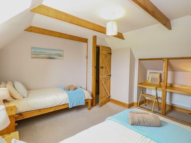 A bedroom with two single beds wooden beams and a small desk with a chair at Dairy Cottage West Caister near Caister-on-Sea