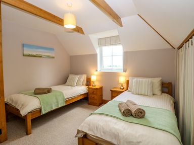 A bedroom with two single beds with green throws and brown towels a window between wooden nightstands with lamps at Dairy Cottage West Caister near Caister-on-Sea