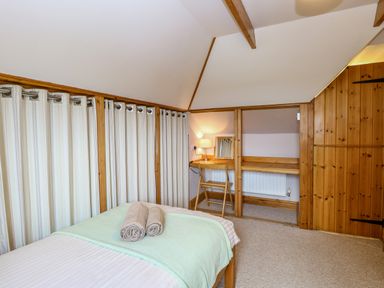 A bedroom with a bed with towels on it curtains along one wall and a wooden desk with a chair and lamp at Dairy Cottage in West Caister near Caister-on-Sea