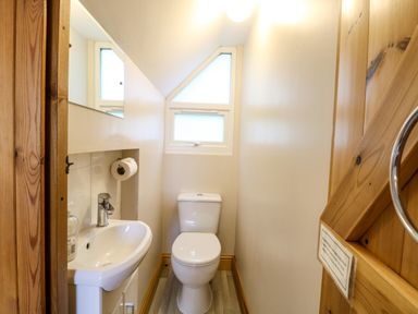 A small bathroom with a toilet and sink under a slanted ceiling with a triangular window at Dairy Cottage West Caister near Caister-on-Sea