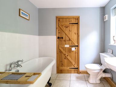 A bathroom with a bathtub a wooden door a toilet and a sink at Dairy Cottage in West Caister near Caister-on-Sea