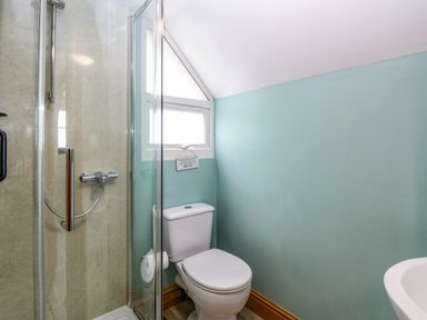 A bathroom with a shower enclosure, a toilet, and a small window at Dairy Cottage in West Caister near Caister-on-Sea
