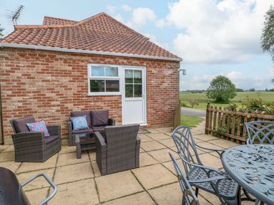 A patio with outdoor seating and table next to a brick house with a tiled roof at Dairy Cottage in West Caister near Caister-on-Sea
