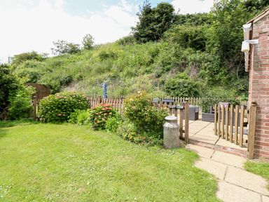 A garden with bushes and flowers a wooden fence and patio furniture at Dairy Cottage in West Caister near Caister-on-Sea
