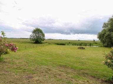 A grassy field with a picnic table pond and trees at Dairy Cottage in West Caister near Caister-on-Sea