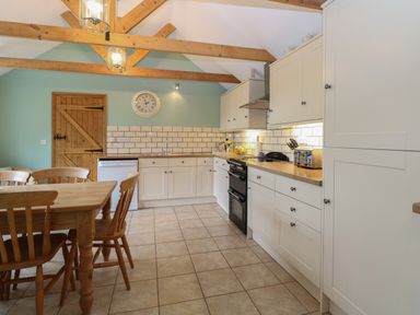 A kitchen with wooden dining table and chairs wooden ceiling beams and white cabinets at Flint Cottage in West Caister near Caister-on-Sea