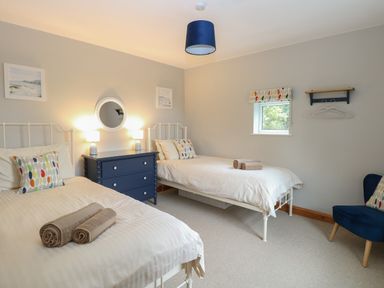 A bedroom with two single beds a blue chest of drawers and a blue chair at Flint Cottage West Caister near Caister on Sea