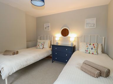 A bedroom with two single beds pillows a blue dresser with two lamps and a round mirror on the wall at Flint Cottage in West Caister near Caister-on-Sea
