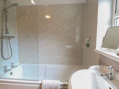 A bathroom with a bathtub shower combination a towel on the tub edge a sink with a faucet and a mirror on the windowsill at Flint Cottage in West Caister near Caister on Sea