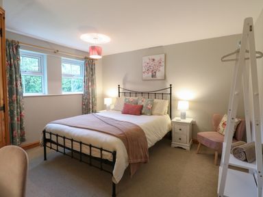 A bedroom with a double bed two bedside tables two lamps a pink chair and floral curtains at Flint Cottage in West Caister near Caister-on-Sea