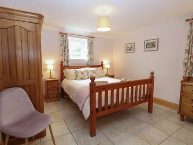 A bedroom with a wooden bed and floral curtains at Flint Cottage in West Caister near Caister on Sea