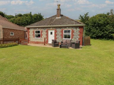 A single-story house with stone and brick exterior a white door two windows and outdoor seating on a lawn at Flint Cottage West Caister near Caister-on-Sea