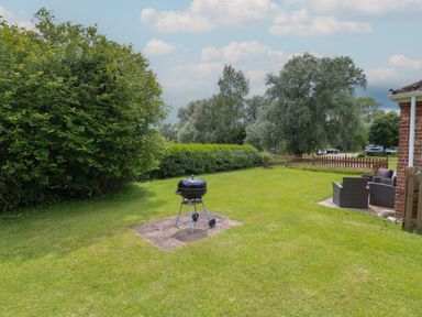 A backyard with a charcoal grill on a stone patio and outdoor seating near a brick building at Flint Cottage in West Caister near Caister-on-Sea