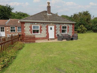 A stone and brick cottage with outdoor seating on a grassy lawn at Flint Cottage in West Caister near Caister-on-Sea