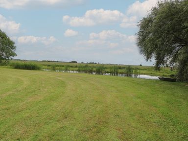 A grassy field with a small pond and trees at Flint Cottage in West Caister near Caister-on-Sea