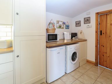 A utility room with a washing machine microwave small fridge wooden door and wall decorations at Flint Cottage in West Caister near Caister-on-Sea