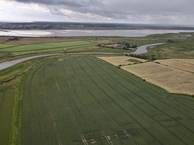 An aerial view of farmland with a river running through it and a body of water in the background at Flint Cottage in West Caister near Caister-on-Sea