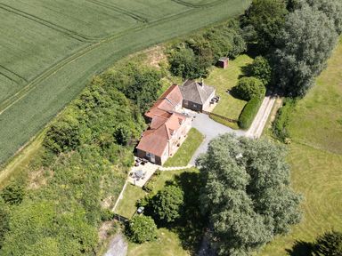 An aerial view of a house with a red tiled roof surrounded by trees grass and farmland at Flint Cottage West Caister near Caister-on-Sea