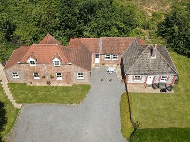 An aerial view of two brick houses with tiled roofs a gravel driveway and green lawns surrounded by trees at Flint Cottage West Caister near Caister-on-Sea