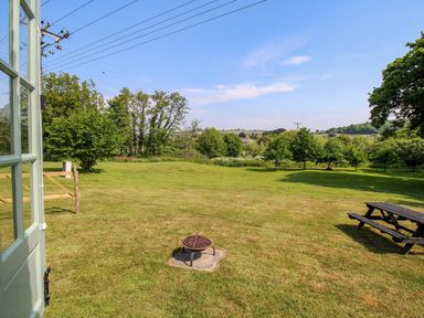 A grassy backyard with a fire pit and a picnic table outside a house at Acres Meadow in Maiden Newton