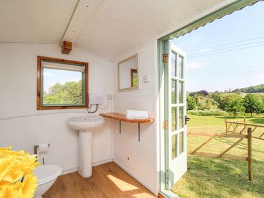 A bathroom with a pedestal sink, toilet, wooden shelf, and open door leading to a garden at Acres Meadow in Maiden Newton
