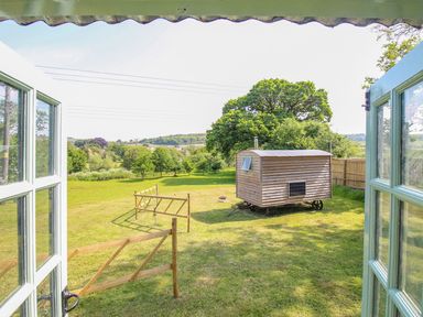A grassy garden with a wooden gate and a shepherd hut viewed through open double doors at Acres Meadow in Maiden Newton