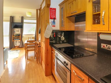 A kitchen with wooden cabinets and an electric stove next to a dining area with a table and chairs at Bluebells in Chapel Stile