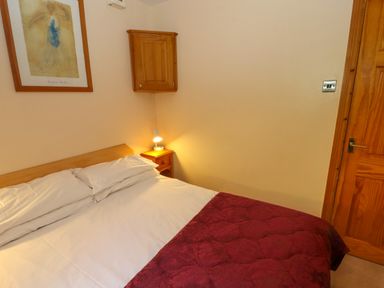 A bedroom with a double bed white sheets red cover and wooden furniture at Bluebells in Chapel Stile