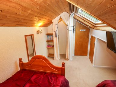 A bedroom with a wooden bed frame a red bedspread a wall mirror bookshelves and a sloped wooden ceiling at Bluebells in Chapel Stile