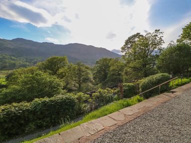 A gravel path with stone edging and a handrail next to bushes and trees with hills in the background at Bluebells in Chapel Stile