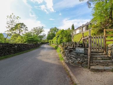 A country road with stone walls and a gate by a house with greenery at Bluebells in Chapel Stile