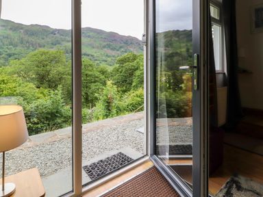 An open glass door leading to a gravel area outside with green trees and hills visible beyond at Bluebells in Chapel Stile