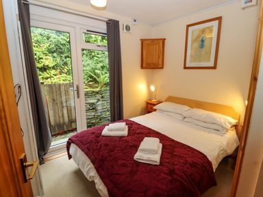 A bedroom with a bed covered in white and red bedding next to glass doors with grey curtains at Bluebells in Chapel Stile