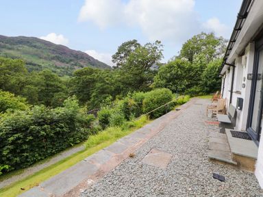 A gravel path with benches outside a white building overlooking green trees and hills at Bluebells in Chapel Stile