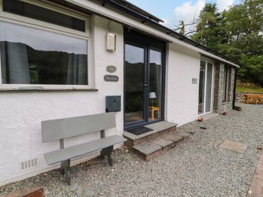 A white building exterior with a gray bench and black double doors at Bluebells in Chapel Stile