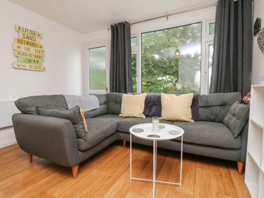 A living room with a grey sectional sofa yellow pillows and a round white table at Number 24 The Park in Kilkhampton