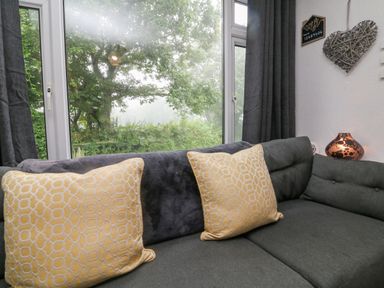 A corner sofa with two yellow patterned cushions and a window with a view of trees at Number 24 The Park in Kilkhampton