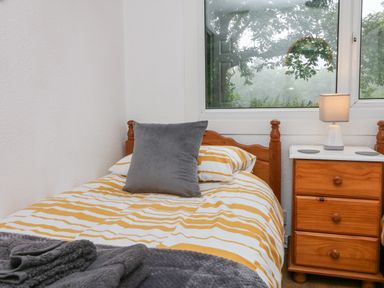 A bedroom with a single bed with striped bedding and a gray pillow next to a wooden nightstand with a lamp at Number 24 The Park in Kilkhampton