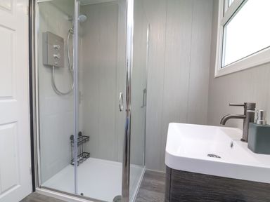 A bathroom with a glass shower enclosure and a sink under a window at Number 24 The Park in Kilkhampton