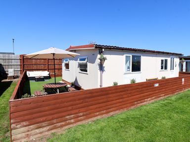A fenced backyard with a picnic table and umbrella next to a single-story house at Sunny South Shore in Bridlington