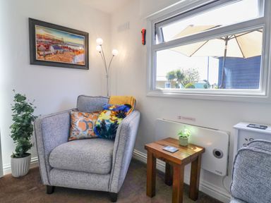 A gray armchair with colorful cushions next to a wooden side table with a plant under a window in a living room at Sunny South Shore in Bridlington