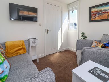 A small living room with two grey sofas a white door a wall mounted television a small white side table and a window at Sunny South Shore in Bridlington